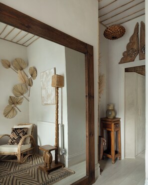 Ein Zimmer mit einem großen Spiegel, einem Korbstuhl, einem kleinen Tisch und Wanddekoration.