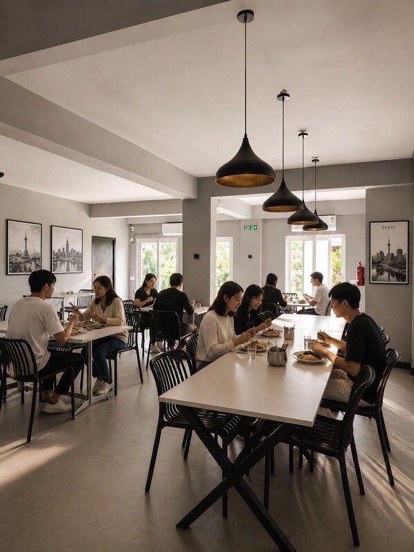 A modern dining area with multiple tables and chairs, pendant lighting, and cityscape artwork on the walls.