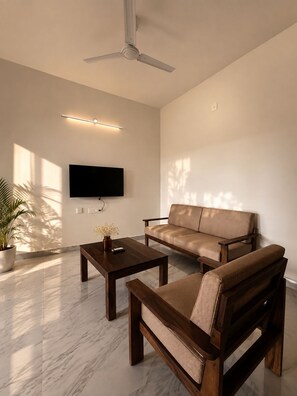 A modern living room with a sofa, a coffee table, a TV mounted on the wall, and a ceiling fan. - Manzl Collective - Palm (Tada Khandrika)