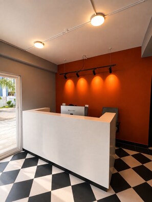 A reception desk with a check-in counter, a wall-mounted light fixture, and a check-in station with a computer. - Manzl Collective - Palm (Tada Khandrika)