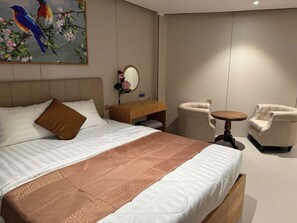 Une chambre d’hôtel avec un grand lit, une table de chevet, une table ronde, deux fauteuils et un tableau représentant des oiseaux accroché au mur.
