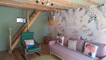Ein gemütliches Wohnzimmer mit einem grünen Sessel, einer Couch, einer Holztreppe und blumigem Wandpapier.