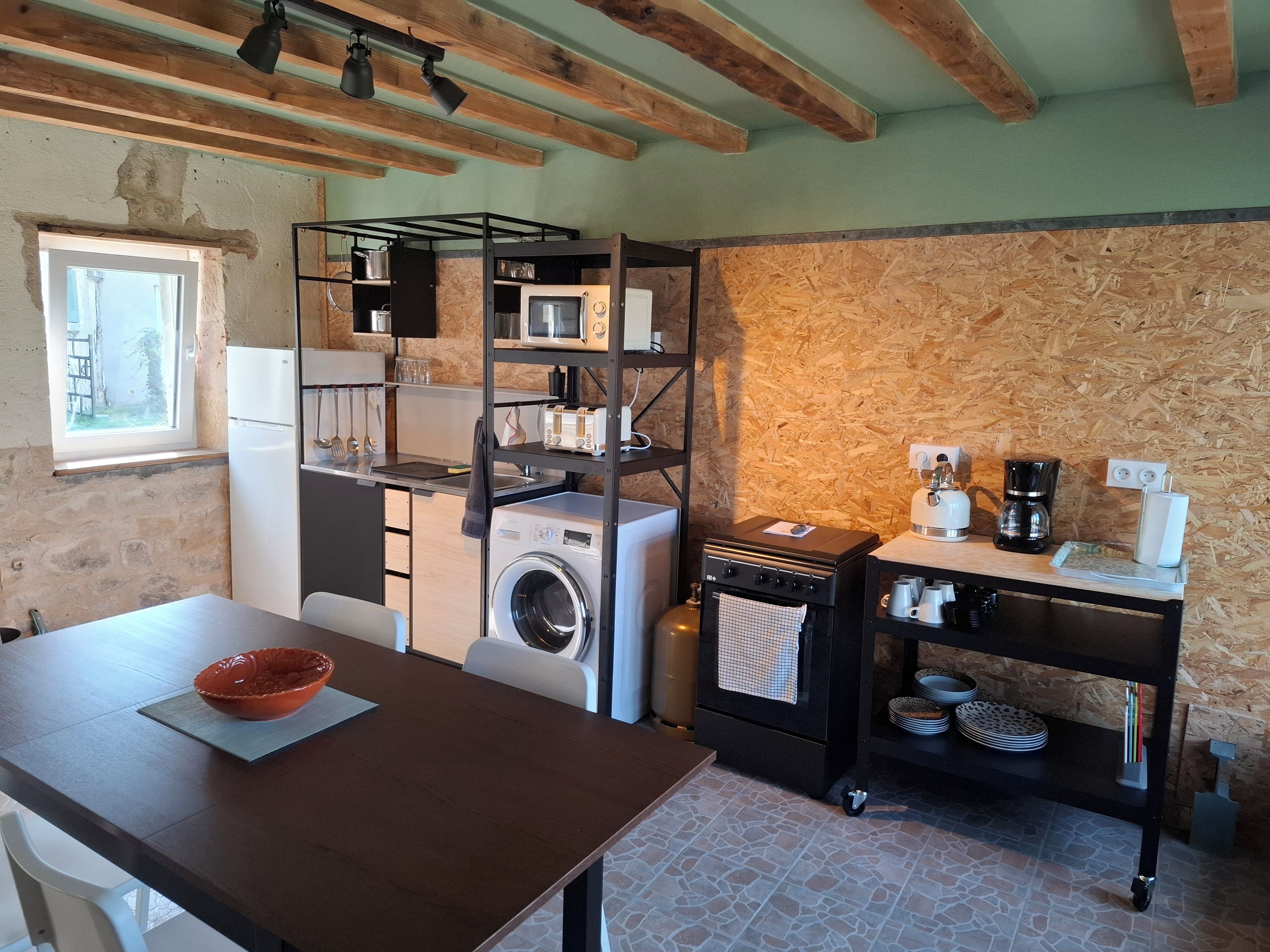 Cocina compacta con lavadora, cafetera y un pequeño comedor con mesa y sillas.