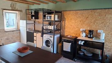 Cocina compacta con lavadora, cafetera y un pequeño comedor con mesa y sillas.