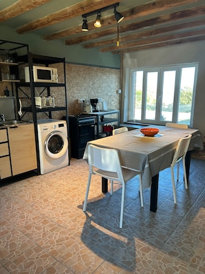 Een functionele keuken met een wasmachine, een koffiezetapparaat en een eettafel met stoelen.