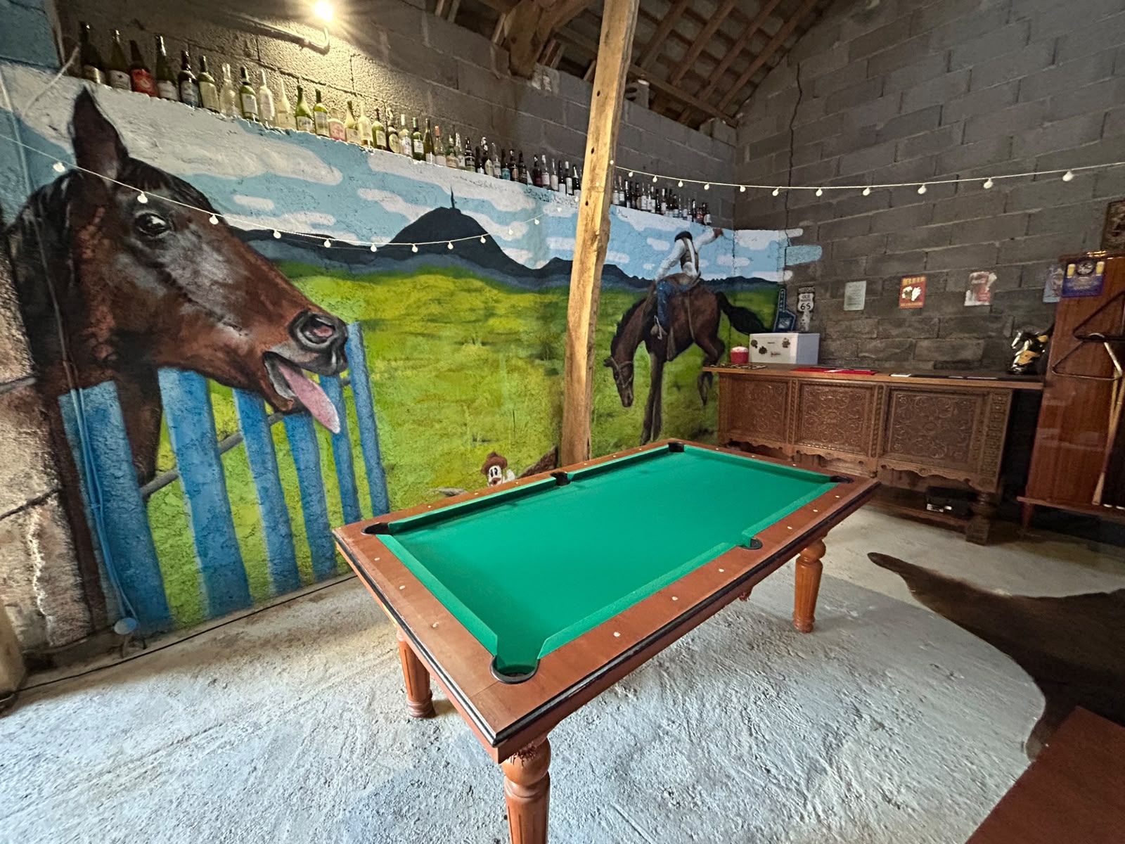 Een pooltafel in een ruimte met een muurschildering van een paard, een bar met flessen en een rustiek plafond.