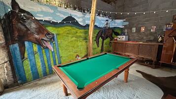 Een pooltafel in een ruimte met een muurschildering van een paard, een bar met flessen en een rustiek plafond.
