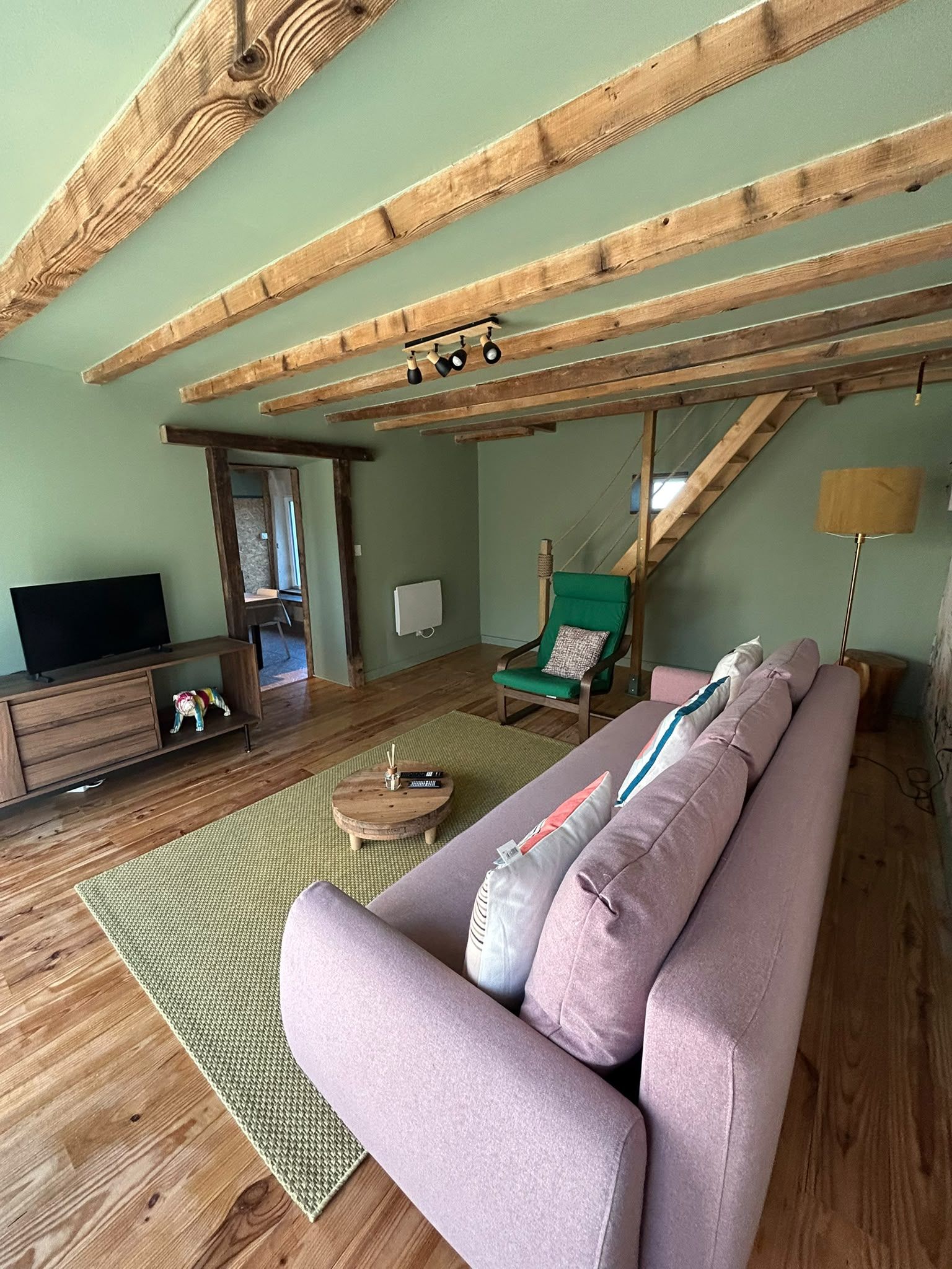 Tunnelmallinen olohuone, jossa on puinen katto, sohva, televisio ja lamppu.