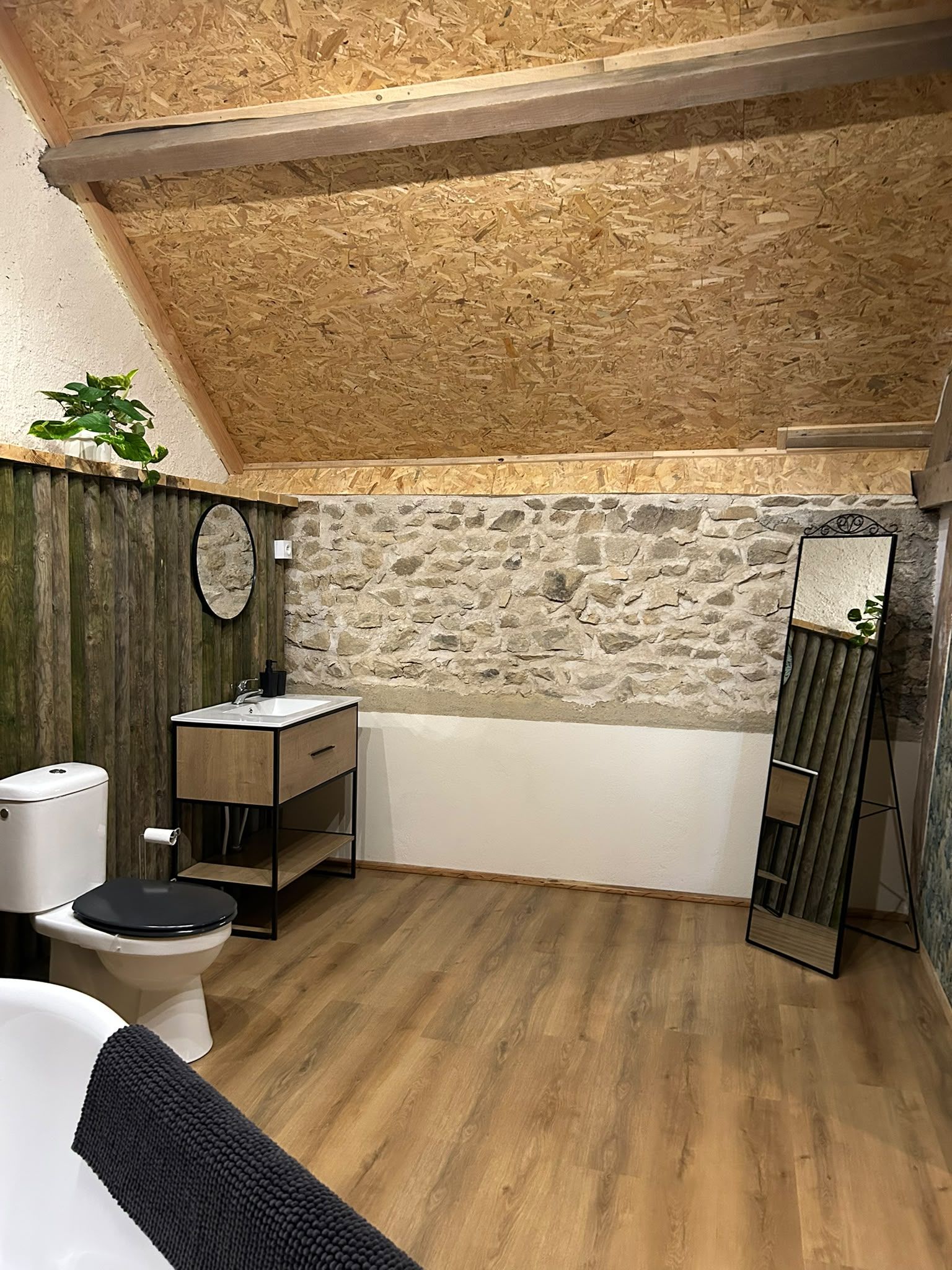 Een badkamer met een stenen muur, een houten vloer en een bad.