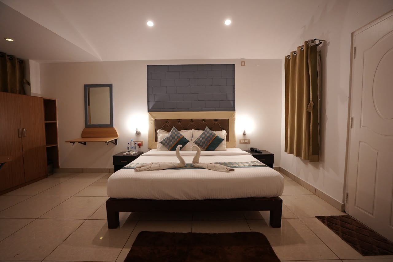 A hotel room with a large bed, bedside tables, a wardrobe, a mirror, and a window with curtains.