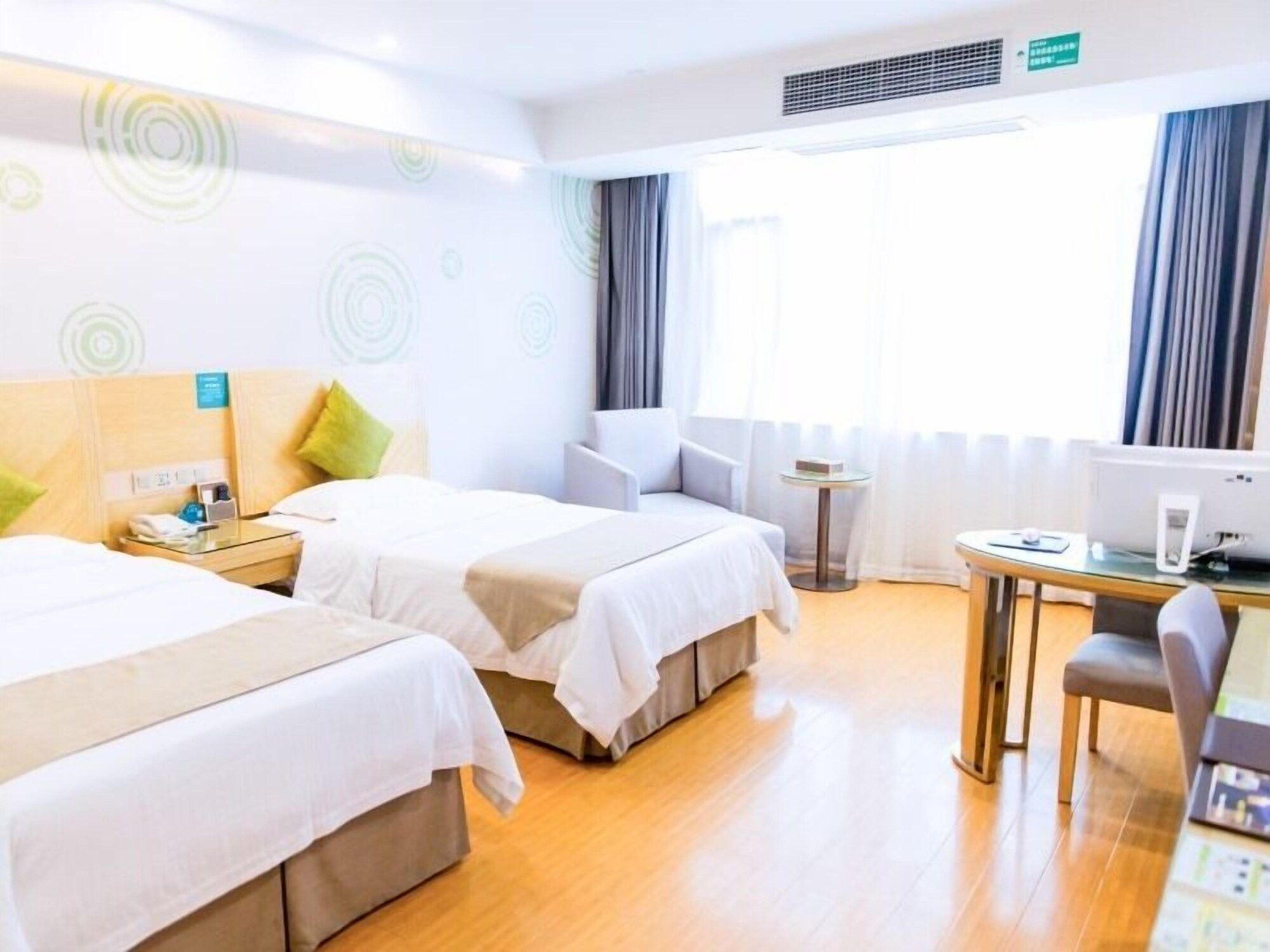 Ein Hotelzimmer mit zwei Betten, einem Schreibtisch, einem Stuhl, einem kleinen Tisch und einem Fenster mit Vorhängen.