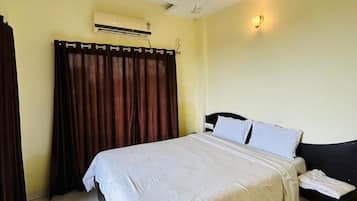 Habitación de hotel con cama, mesita de noche, ventilador de techo, aire acondicionado y cortina.