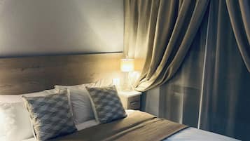 Ett hotellrum med en säng, en takfläkt, ett nattduksbord med en lampa och ett fönster med gardiner.