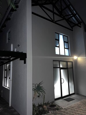 A two-story building with a large glass door entrance, a small garden with a palm tree, and a metal roof structure.