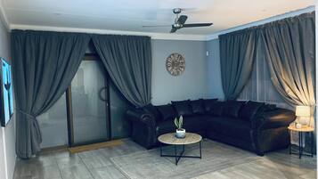 A living room with a black leather sofa, a round coffee table, a wall clock, and a ceiling fan.