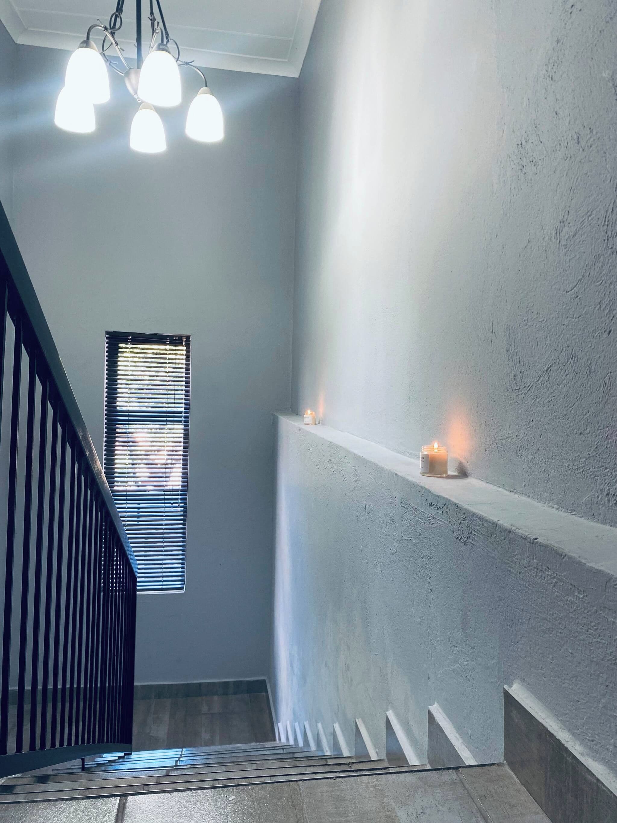 A staircase with a railing, a window with blinds, and a wall-mounted shelf with candles.