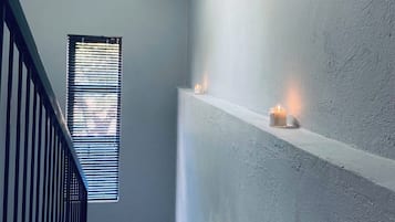 A staircase with a railing, a window with blinds, and a wall-mounted shelf with candles.