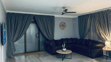 A living room with a black leather sofa, a round coffee table, a potted plant, a wall clock, and a ceiling fan.