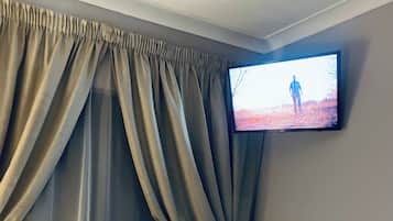 Una habitación de hotel con una cama, un televisor montado en la pared y un ventanal con cortinas.