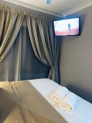 Una habitación de hotel con una cama, un televisor montado en la pared y un ventanal con cortinas.