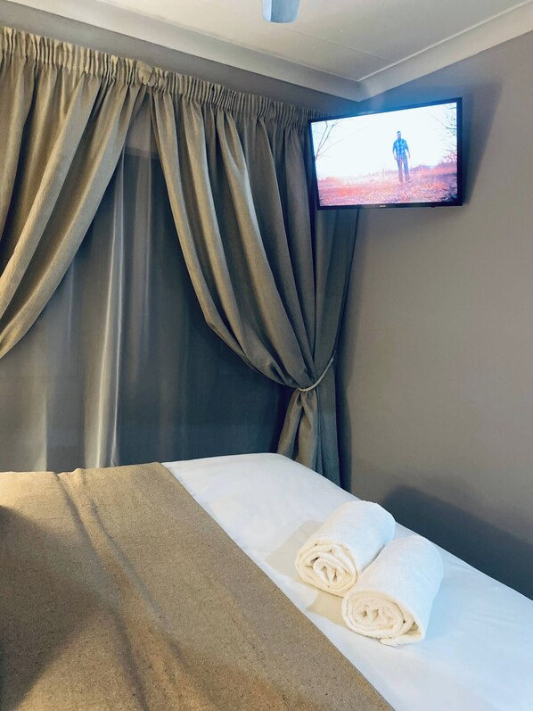 A hotel room with a bed, a television mounted on the wall, and a window with curtains.