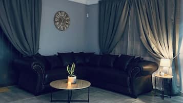 Una sala de estar moderna con un sofá seccional, una mesa de centro redonda con una planta, un ventilador de techo y un reloj en la pared.