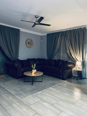 A modern living room with a sectional sofa, a round coffee table with a plant, a ceiling fan, and a clock on the wall.
