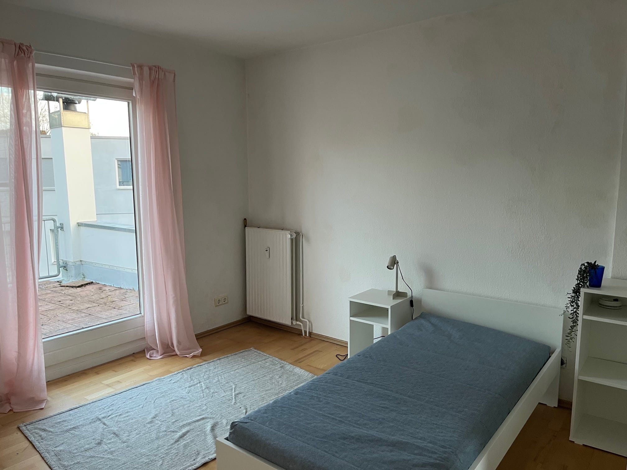 Ein Schlafzimmer mit einem Einzelbett, einem Heizkörper, einem Schreibtisch und einem Fenster mit Vorhängen.