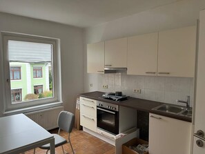 Eine kleine Küche mit Fenster, einem Herd, einer Spüle und Schränken.