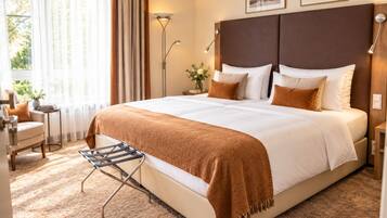 A hotel room with a large bed, a side table, a chair, a floor lamp, and a window with curtains.