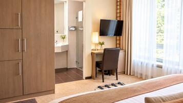 A hotel room with a bed, a desk with a chair, a television, and a bathroom visible through an open door.