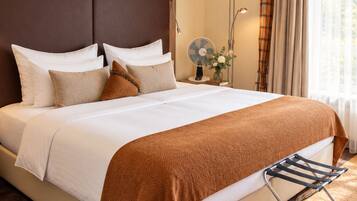 A hotel room with a large bed, a bedside lamp, a fan, and a window with curtains.