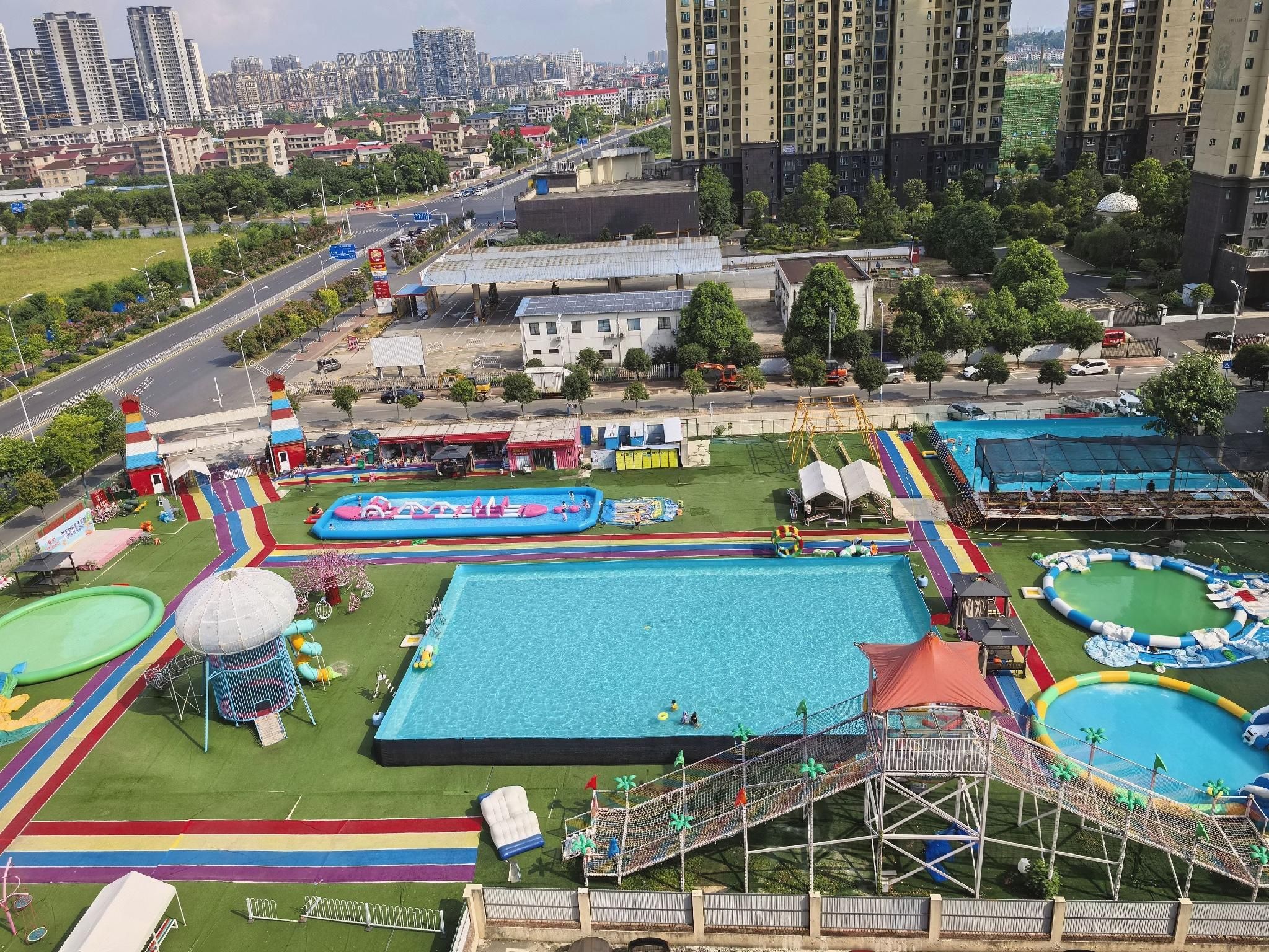 Una gran piscina al aire libre con múltiples toboganes acuáticos y zonas de juegos, rodeada de vegetación y edificios.