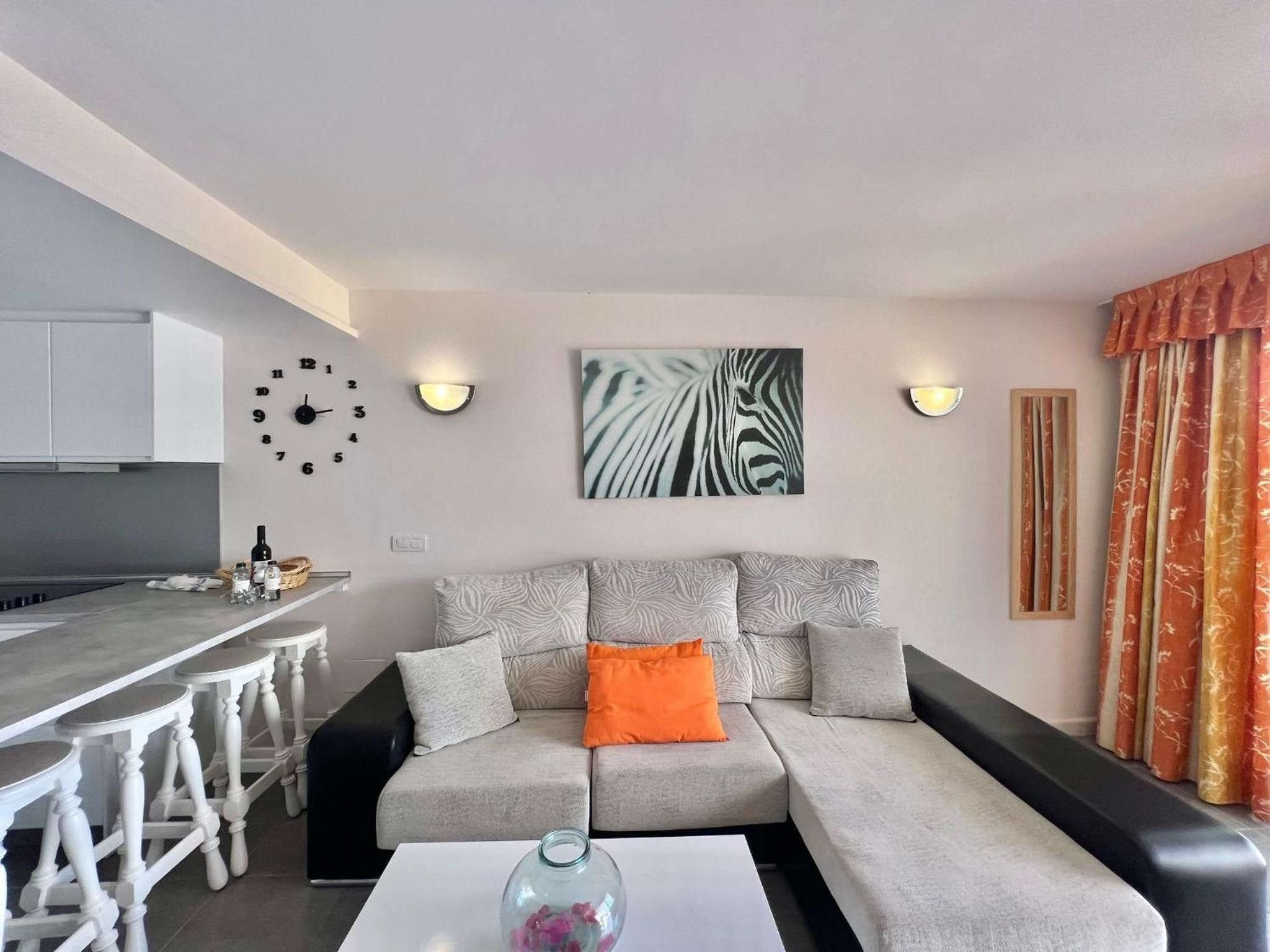 En moderne stue med en grå sofa, et hvidt sofabord og et køkkenområde med en bar.