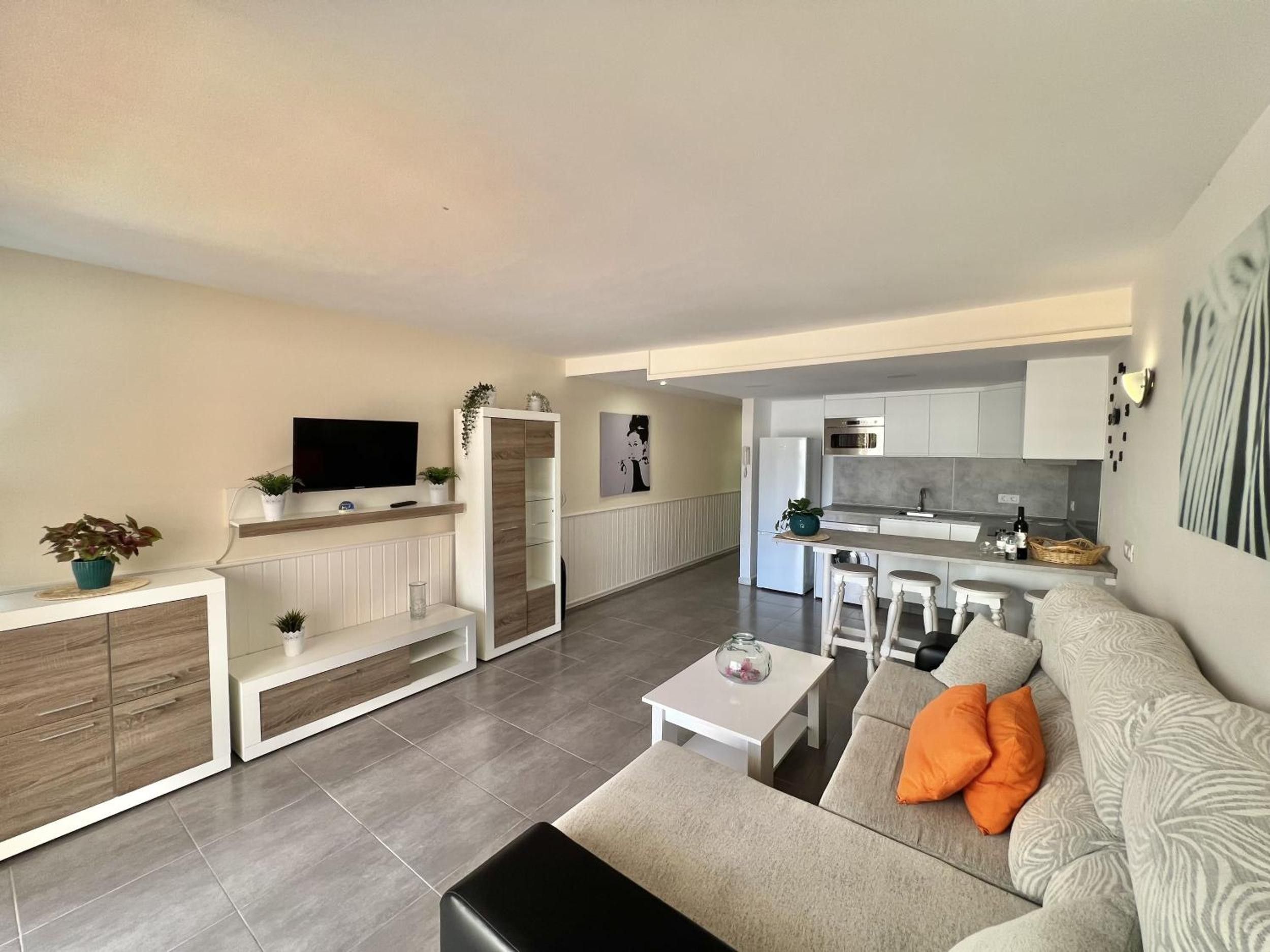 Een moderne woonkamer met een bank, salontafel en televisie. Er is een keukenhoek met een eettafel en stoelen.