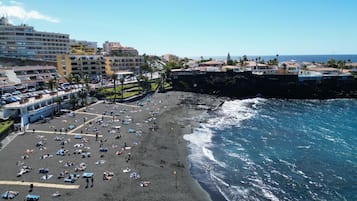 A beach with numerous sun loungers and umbrellas, a rocky shoreline, and buildings in the background.