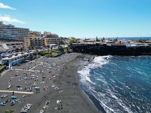 A beach with numerous sun loungers and umbrellas, a rocky shoreline, and buildings in the background. - Apartment 'Neptuno Pool&Beach By Sydney' with Communal Pool, Private Terrace and Wi-Fi (La Arena)
