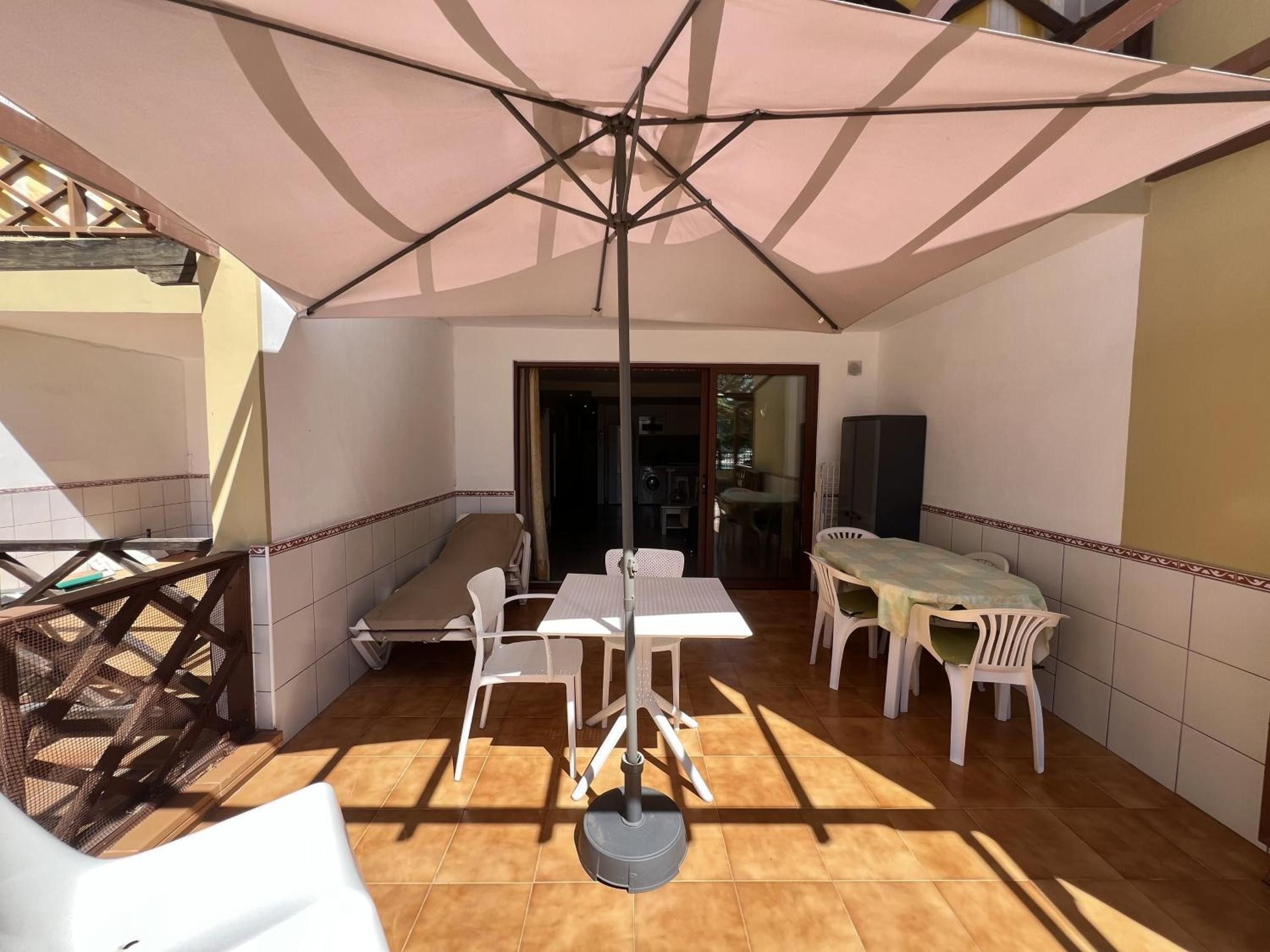 Un patio coperto con tavolo e sedie, una ventola a soffitto e vista sull'interno della casa.
