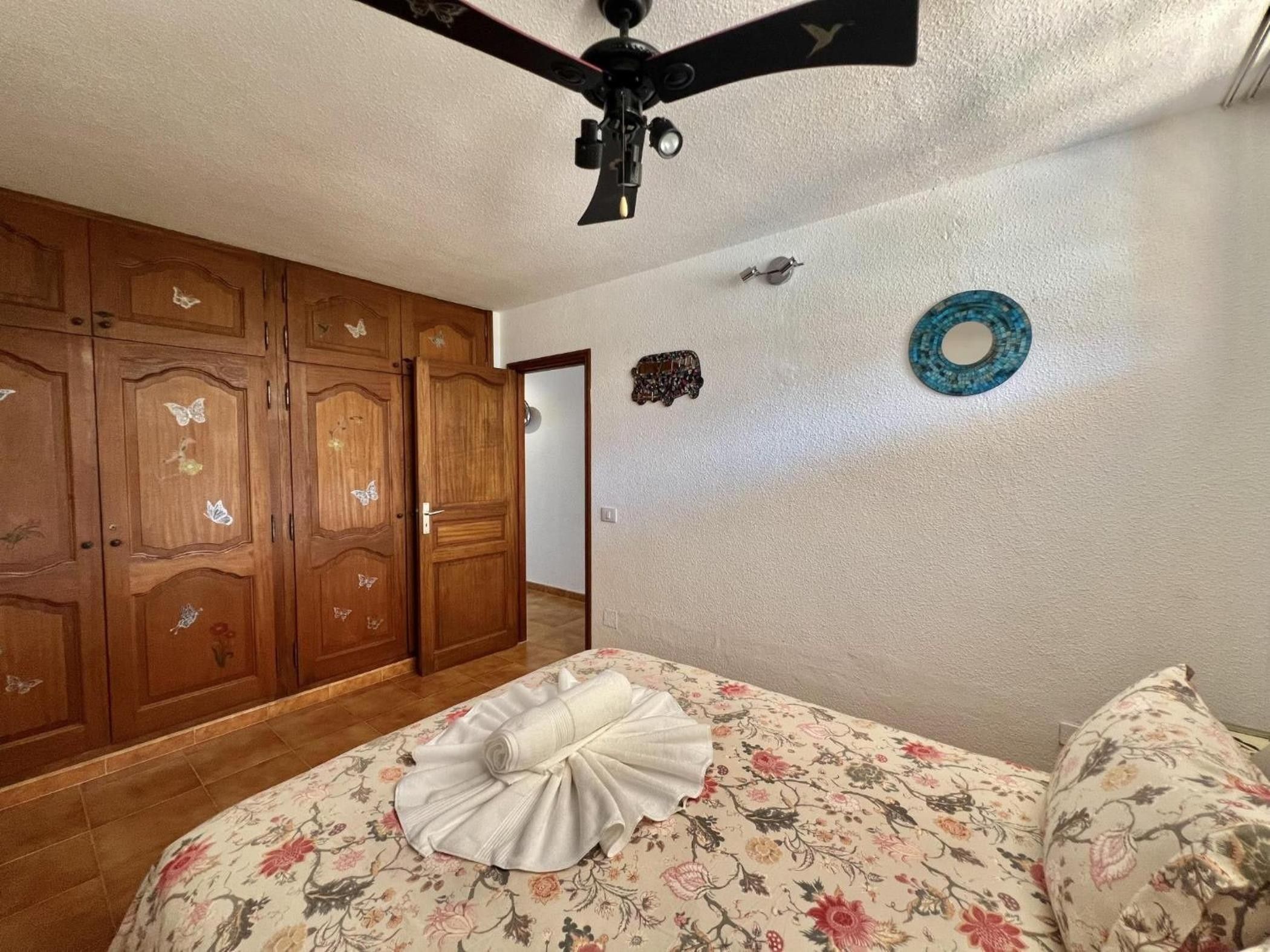 Ein Schlafzimmer mit Bett, Holzschrank, Deckenventilator und dekorativen Wandelementen.
