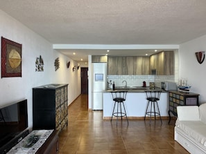 Cocina moderna con una isla central, taburetes de bar y una zona de comedor con un sofá blanco.