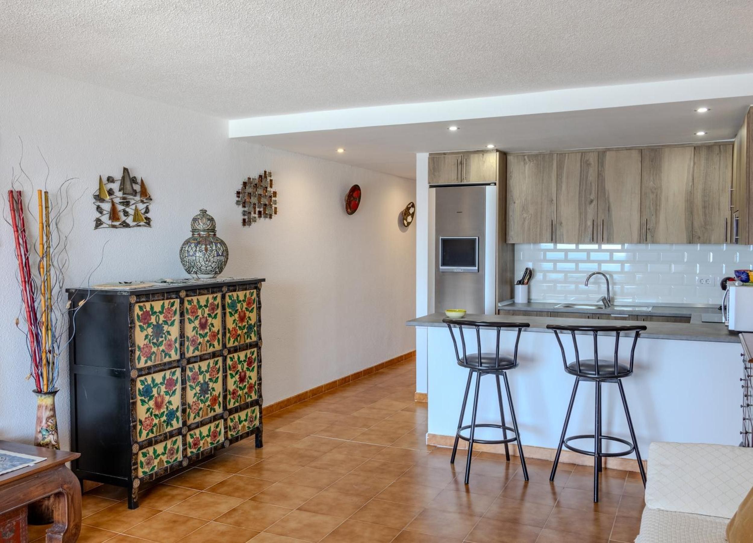 Una cocina moderna con una isla central, taburetes de bar y un mueble decorativo.
