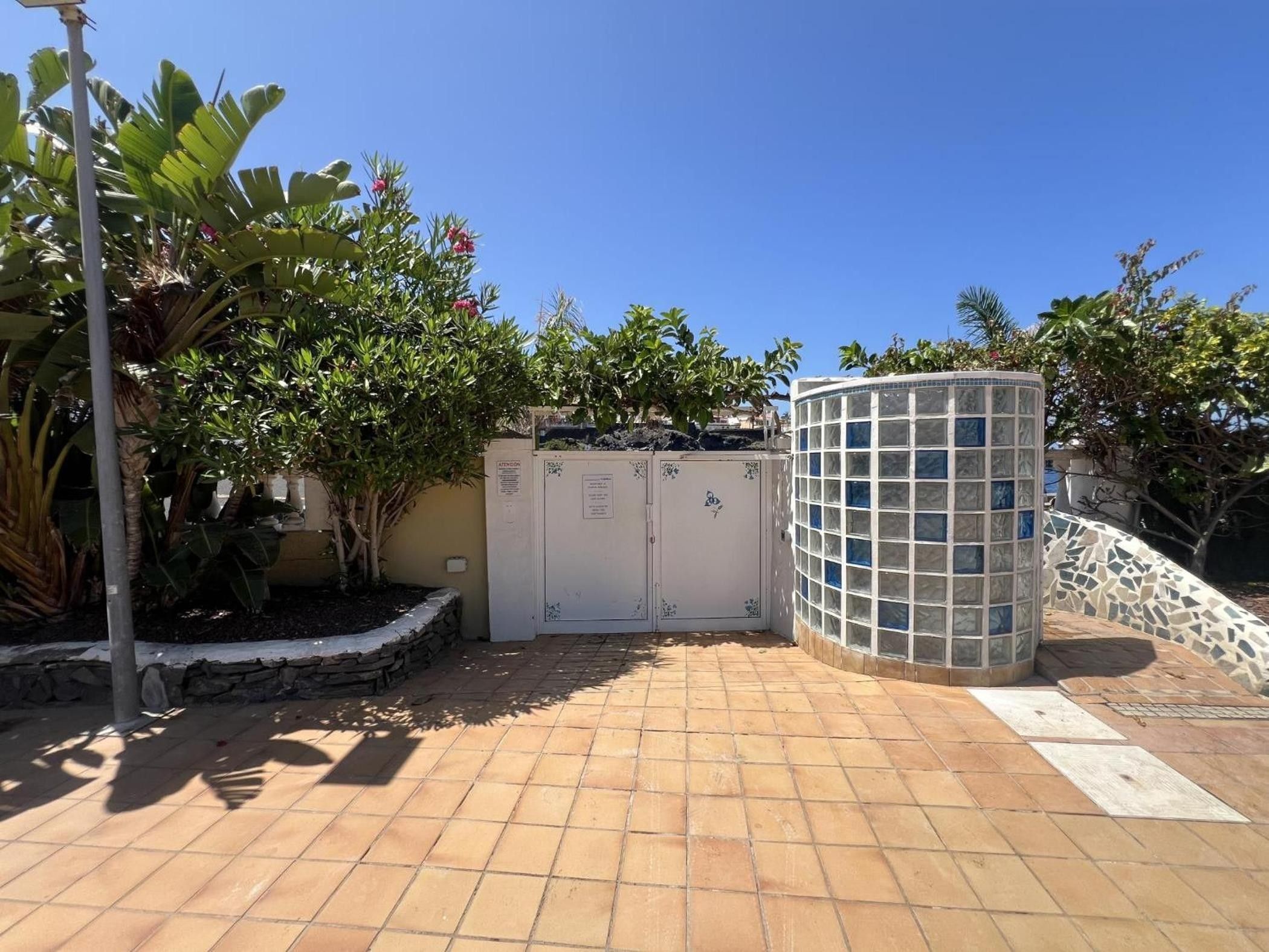 A gated entrance with a tiled patio, a stone wall, and a decorative glass structure.