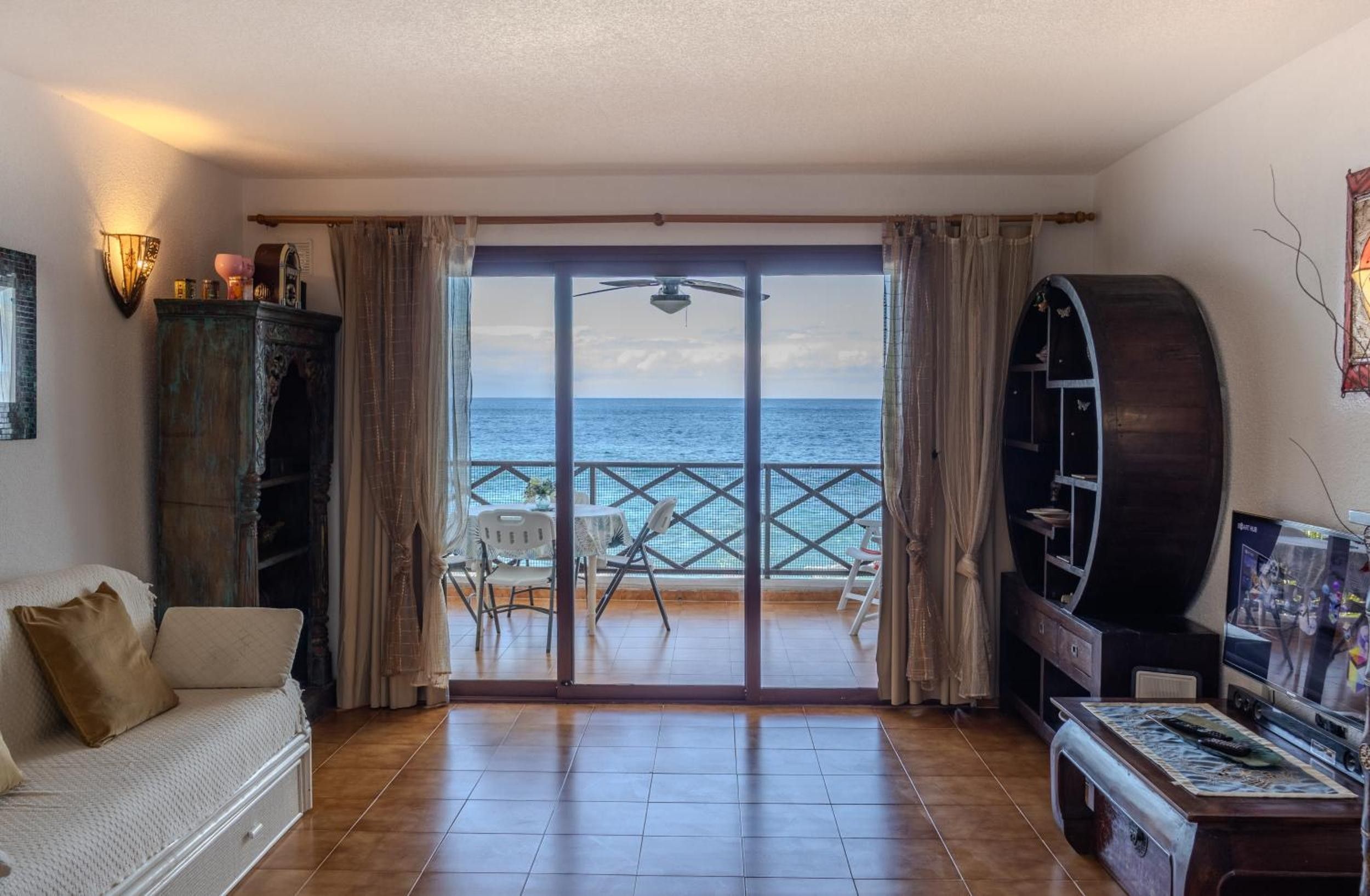 Een woonkamer met uitzicht op zee, een plafondventilator, een televisie en een bank.