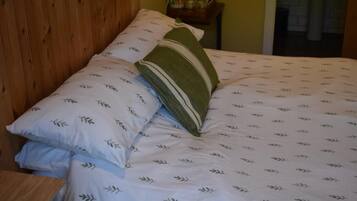 A bed with patterned bedding and pillows, a wooden headboard, and a small bedside table with items on it.