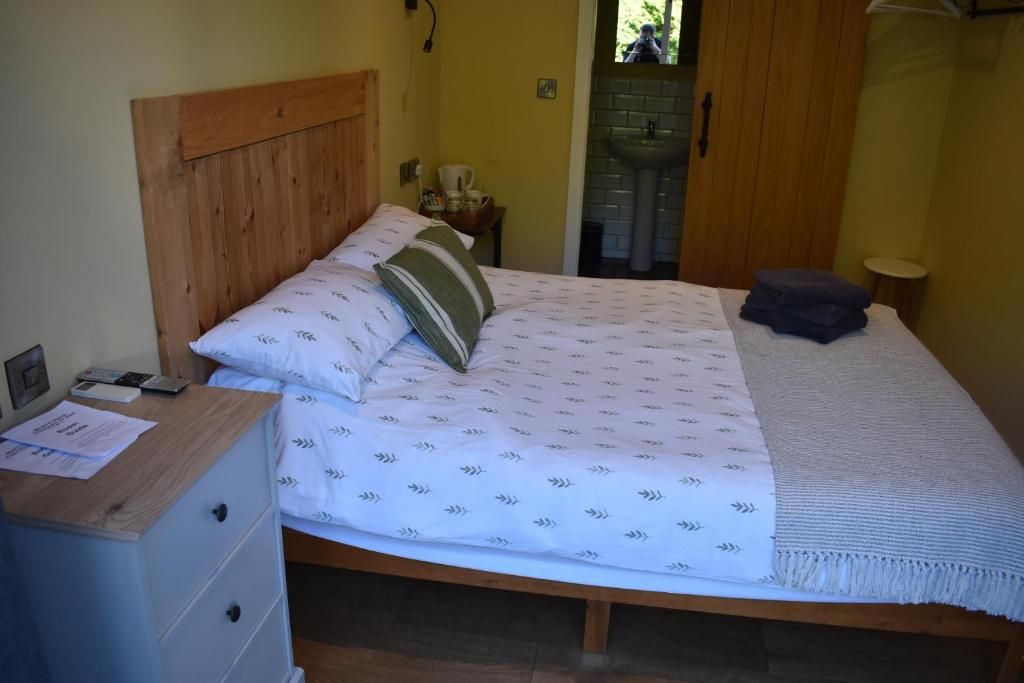 Un lit simple avec une tête de lit en bois, une table de chevet avec une lampe et une petite table de chevet sur laquelle se trouvent une tasse et un livre.