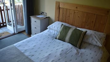 A bedroom with a wooden headboard, a bed with patterned bedding, a nightstand with a lamp, and a view of a wooden fence through a sliding door.