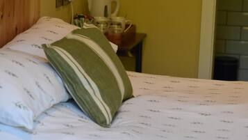A bed with patterned bedding and pillows, a wooden headboard, and a small table with a kettle and cups.
