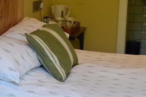 Una cama con ropa de cama y almohadas estampadas, un cabecero de madera y una mesita con hervidor y tazas.