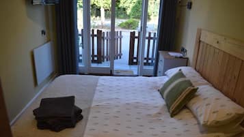 A hotel room with a bed, a nightstand, a TV mounted on the wall, and a view of the outside through a sliding glass door.