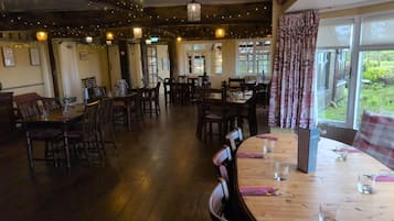 A restaurant with multiple tables and chairs, wooden flooring, and string lights on the ceiling.